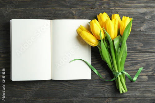 Beautiful yellow tulips and notebook on wooden background, space for text. Blogging concept