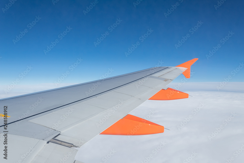 orange airplane wing view from inside plane on air clouds sky