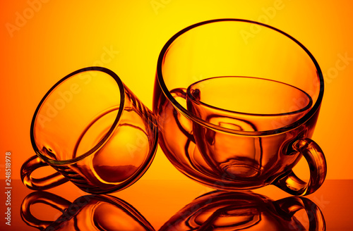 Round-shaped empty glass cups are photographed against the light on an orange background. © Nedilko