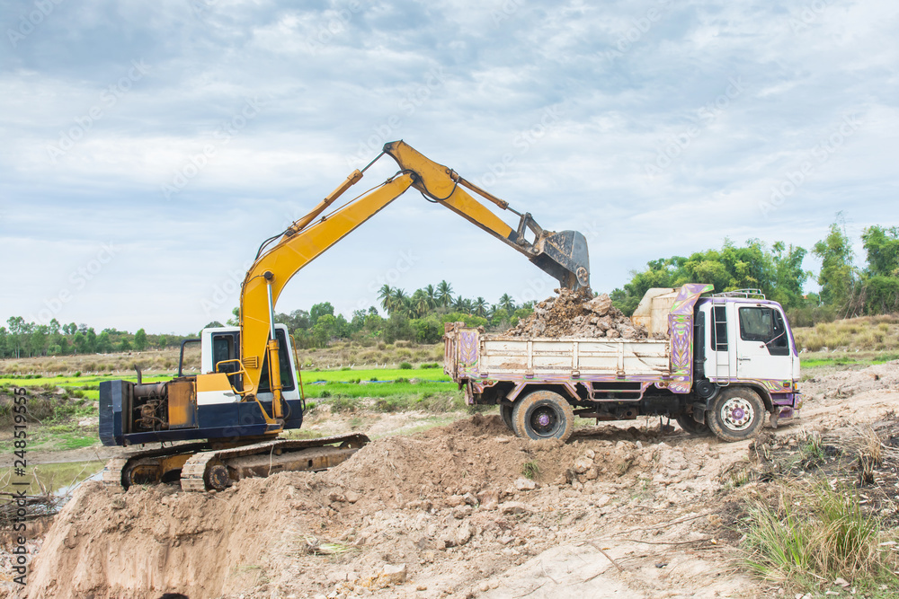 Yellow excavator machine loading soil into a dump truck at construction site Yellow excavator machine loading soil into a dump truck at construction site