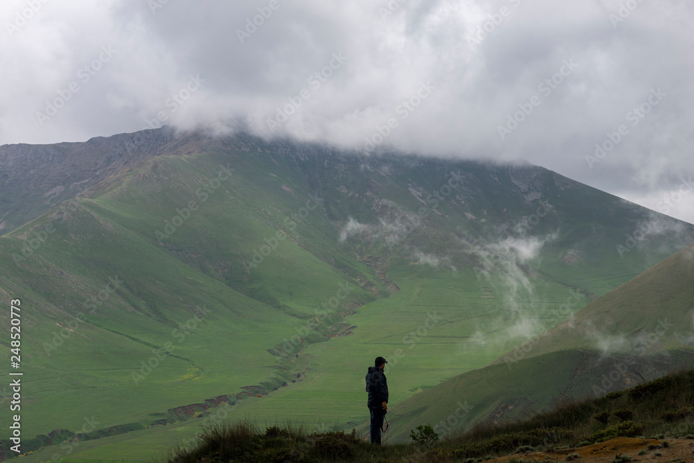 Man standing of the pick and looking at the beautiful mountain. Landscape, mountain in the clouds. Armenia.