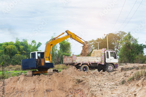 Yellow excavator machine loading soil into a dump truck at construction site