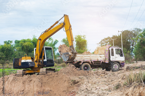 Yellow excavator machine loading soil into a dump truck at construction site