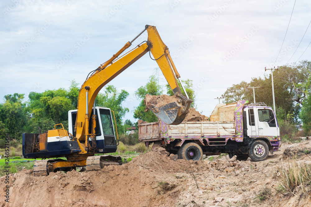 Yellow excavator machine loading soil into a dump truck at construction site