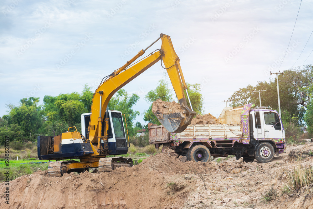 Yellow excavator machine loading soil into a dump truck at construction site Yellow excavator machine loading soil into a dump truck at construction site