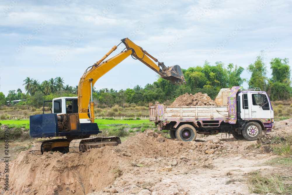 Yellow excavator machine loading soil into a dump truck at construction site Yellow excavator machine loading soil into a dump truck at construction site