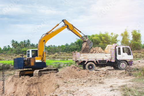 Yellow excavator machine loading soil into a dump truck at construction site