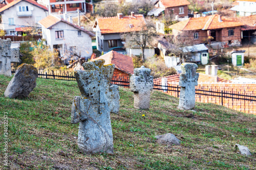 Cross of St. Peter on an old tombstone at the churchyard of St. Petka Eastern Orthodox Church in Tsari Mali Grad fortress, the village of Belchin, Bulgaria in the background photo