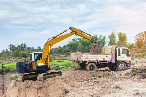 Yellow excavator machine loading soil into a dump truck at construction site