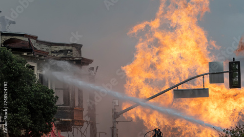 Water from a fire truck plays over a partially burned building in San Francisco.  Flames from a punctured gas main fill the right half of the frame.