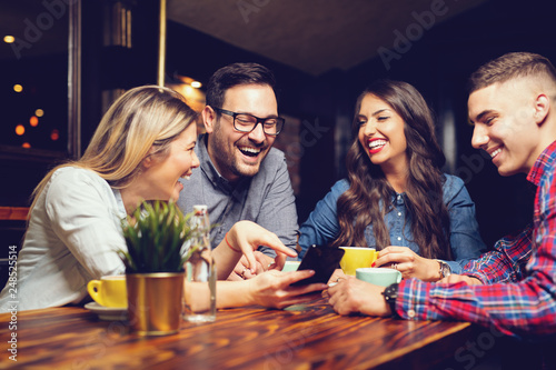 Portrait of cheerful young friends looking at smart phone while sitting in cafe. - Image