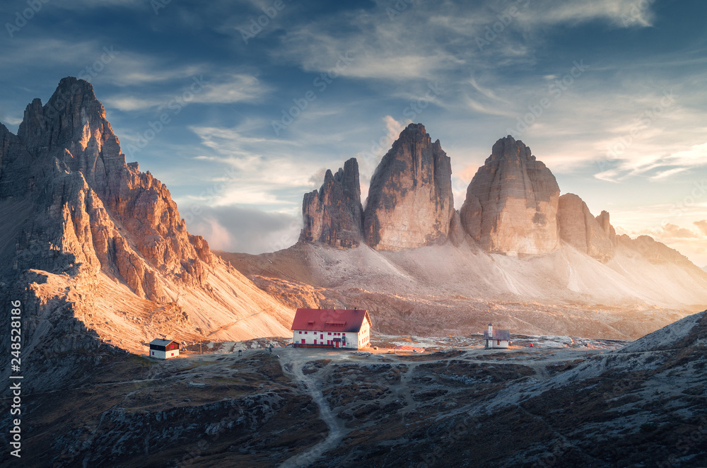 Mountain valley with beautiful house and church at sunset in autumn. Landscape with buildings, high rocks, trail, blue sky and sunlight. Mountains in Tre Cime park in Dolomites, Italy. Italian alps  - obrazy, fototapety, plakaty 