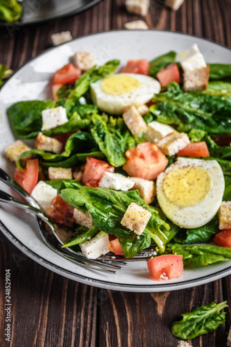 Fresh vegetable salad with tomatoes, spinach, bread crumbs, egg and feta. Healthy food. Dietary dinner or lunch menu. Salad plate on the table.