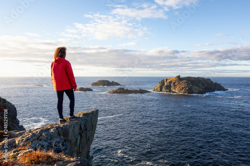 Wallpaper Mural Woman in red jacket is standing at the edge of a cliff and enjoying the beautiful ocean scenery