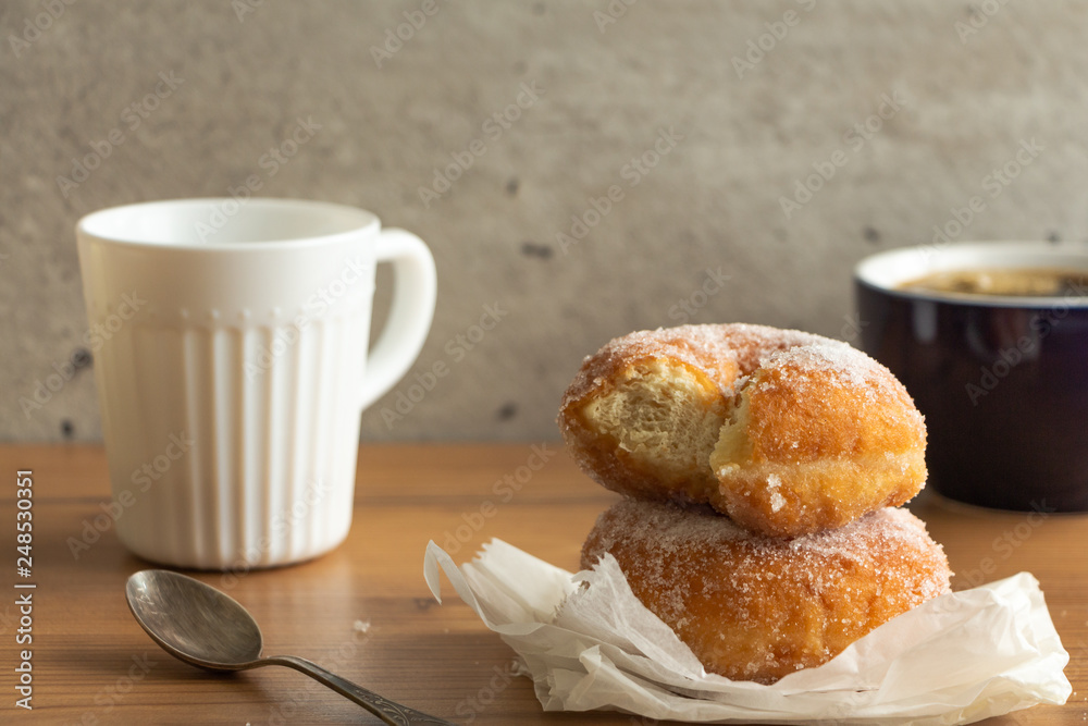 Sugar coated doughnuts on crumpled paper with a two cups of coffee , on wooden tabletop. Sugar coated doughnuts on crumpled paper with a two cups of coffee , on wooden tabletop.