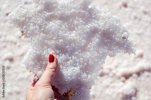 Female hand holding natural salt crystals on the background of a salt lake, side view close up