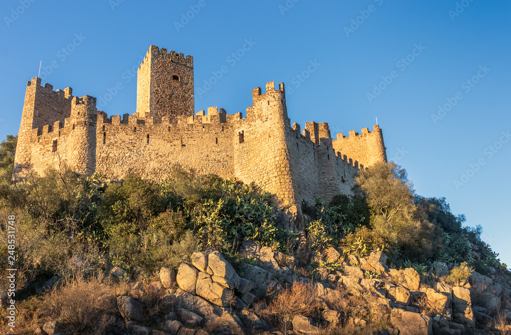 12th century Almourol castle lit by the late afternoon sun with blue sky.