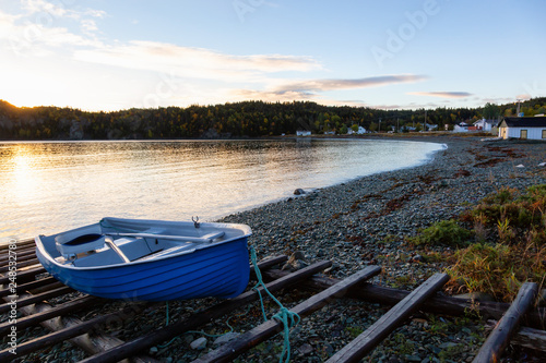 Wooden boat laying by the Atlantic Ocean Shore during a vibrant sunrise. Taken in Beachside, Newfoundland, Canada.