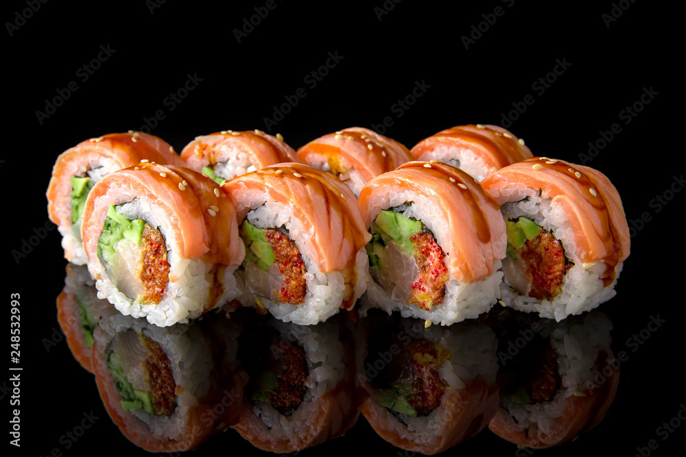 Sushi roll (Geisha) with fire-scorched salmon, sea bass, shrimp, avocado scallop, caviar, philadelphia cheese, unagi sauce on black background. Sushi menu. Japanese food. Sushi roll (Geisha) with fire-scorched salmon, sea bass, shrimp, avocado scallop, caviar, philadelphia cheese, unagi sauce on black background. Sushi menu. Japanese food.