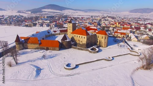 Camera flight over snowy landscape near Svihov village with ancient castle. Gothic architecture on river island. Beautiful landmark in national park Sumava. Winter season in Czech Republic. photo