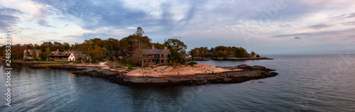 Panoramic seascape view of beautiful homes on a rocky Atlantic Coast during a vibrant sunset. Taken in New Haven, Connecticut, United States.