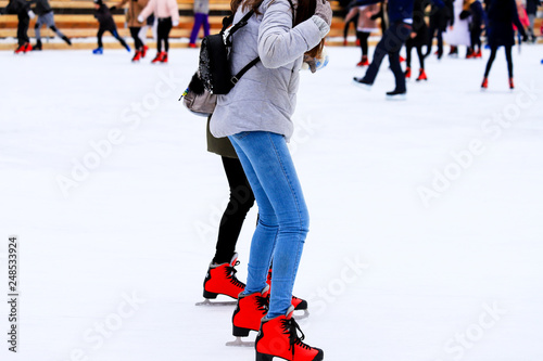 Winter rink. The girl in the red skates riding on the ice. Active family sport during the winter holidays and the cold season. School sports clubs