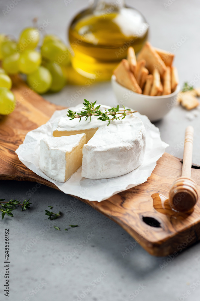 Brie cheese or camembert on cheese platter with crackers, grapes, olive oil. Closeup view, selective focus