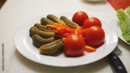 Marinated cucumbers and red tomatoes in a white plate, isolated close-up