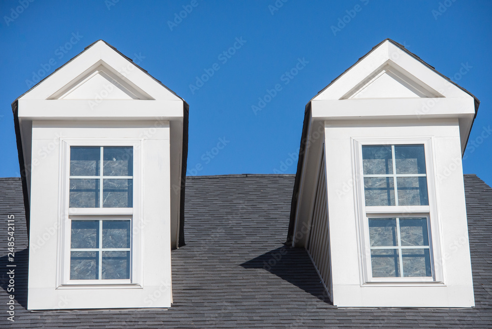 Double white dormer sash window with blue sky background on a gable roof with vinyl siding on a luxury estate house in the East Coast of the USA for upper middle class families Double white dormer sash window with blue sky background on a gable roof with vinyl siding on a luxury estate house in the East Coast of the USA for upper middle class families