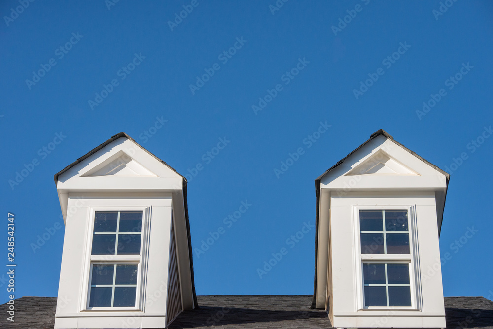 Double white dormer sash window with blue sky background on a gable roof with vinyl siding on a luxury estate house in the East Coast of the USA for upper middle class families Double white dormer sash window with blue sky background on a gable roof with vinyl siding on a luxury estate house in the East Coast of the USA for upper middle class families