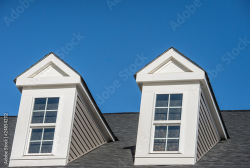 Double white dormer sash window with blue sky background on a gable roof with vinyl siding on a luxury estate house in the East Coast of the USA for upper middle class families photo