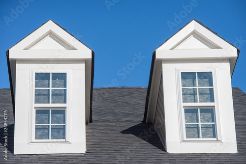 Double white dormer sash window with blue sky background on a gable roof with vinyl siding on a luxury estate house in the East Coast of the USA for upper middle class families