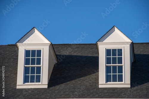 Double white dormer sash window with blue sky background on a gable roof with vinyl siding on a luxury estate house in the East Coast of the USA for upper middle class families