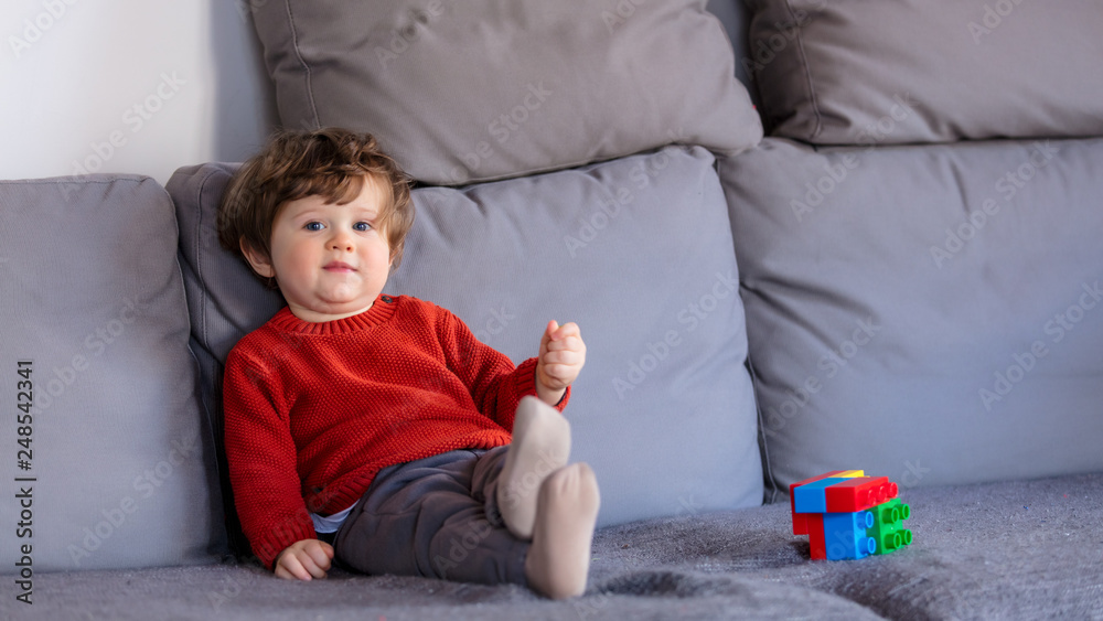 Funny little boy sitting on sofa in red sweater Funny little boy sitting on sofa in red sweater