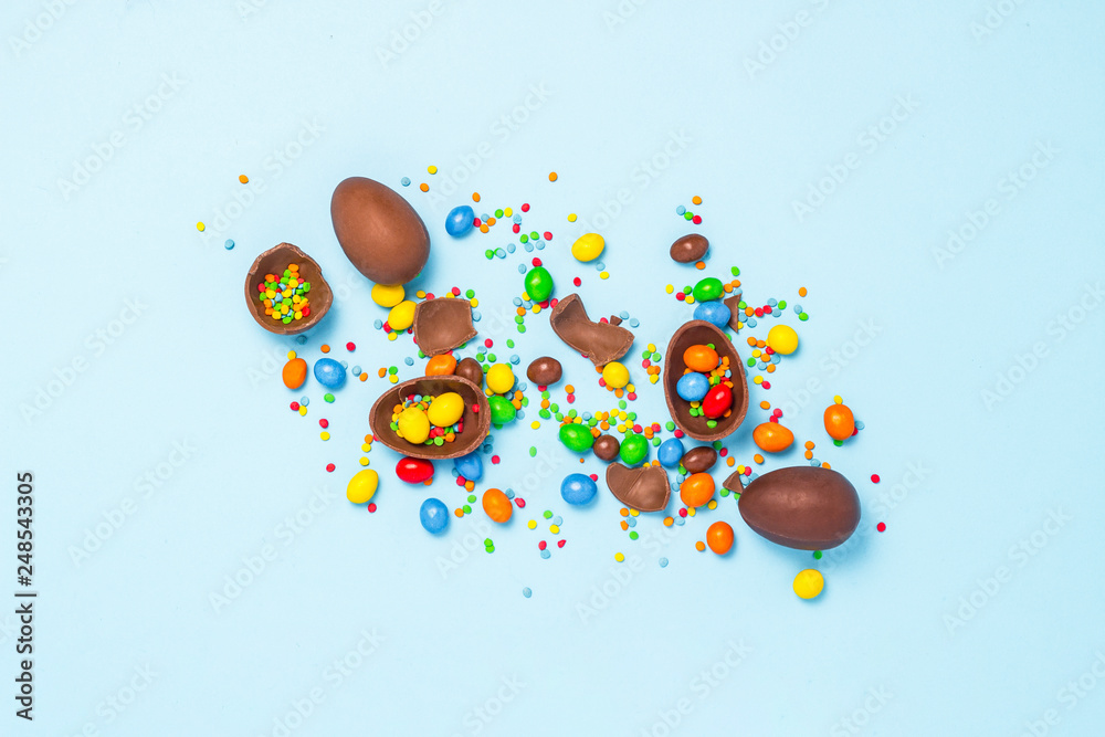 Broken and whole chocolate Easter eggs, multicolored sweets on blue background. Concept of celebrating Easter, Easter decorations, search for sweets for Easter Bunny. Flat lay, top view. Copy Space