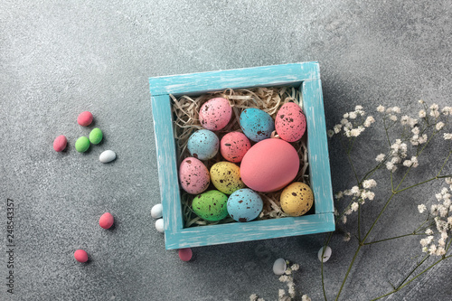 Colorful easter eggs in box and flowers on table. Top view with copy space.