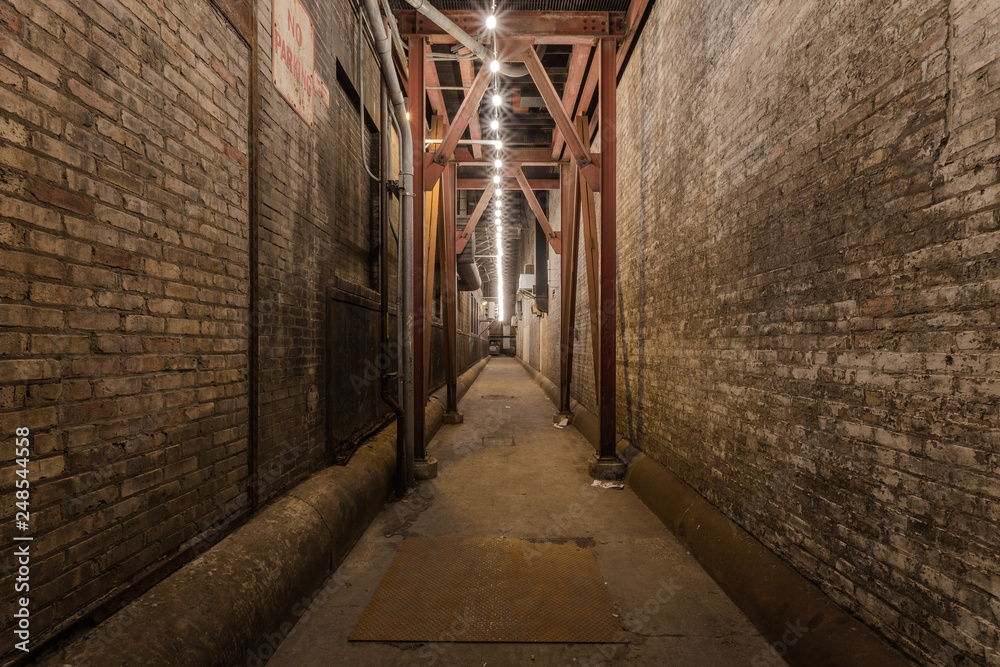 Looking down an urban alleyway with brick buildings, steel beams and a string of light bulbs