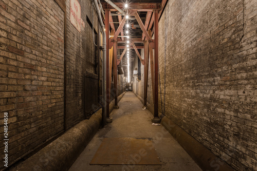 Looking down an urban alleyway with brick buildings  steel beams and a string of light bulbs
