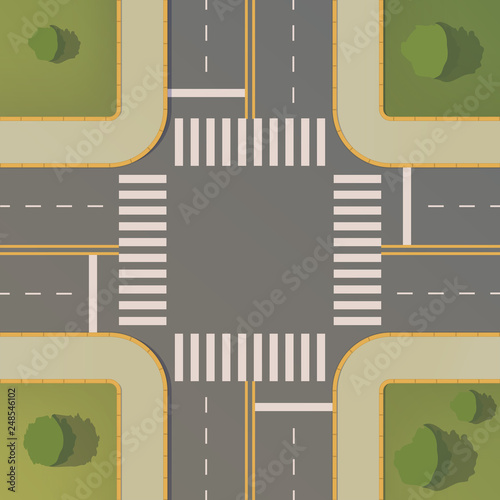 Crossroads of two roads with pedestrian paths, curbs and boards, road markings, grass, bushes and trees.