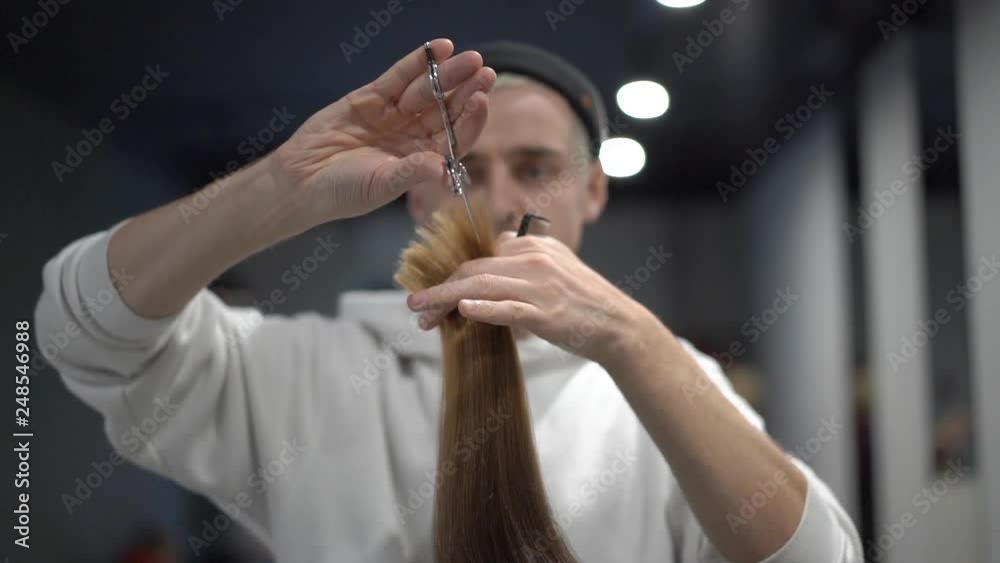 A male hairdresser milling a lock of a brown hair and combing it A male hairdresser milling a lock of a brown hair and combing it
