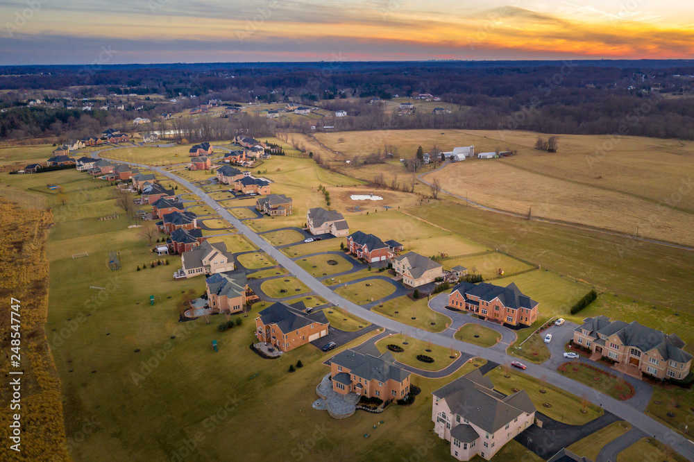 Obraz premium Aerial sunset view of American luxury traditional, contemporary single family home estates with gable roof, in a new residential suburban neighborhood, for upper middle class families in the USA
