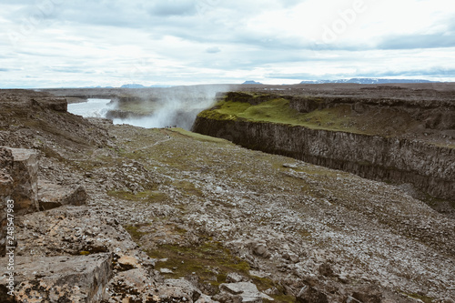 View to river of Dettifoss waterfall and mountains, rocks in the foreground, river is in perspective, Iceland, summer