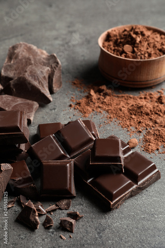 Pieces of chocolate and cocoa powder on grey background