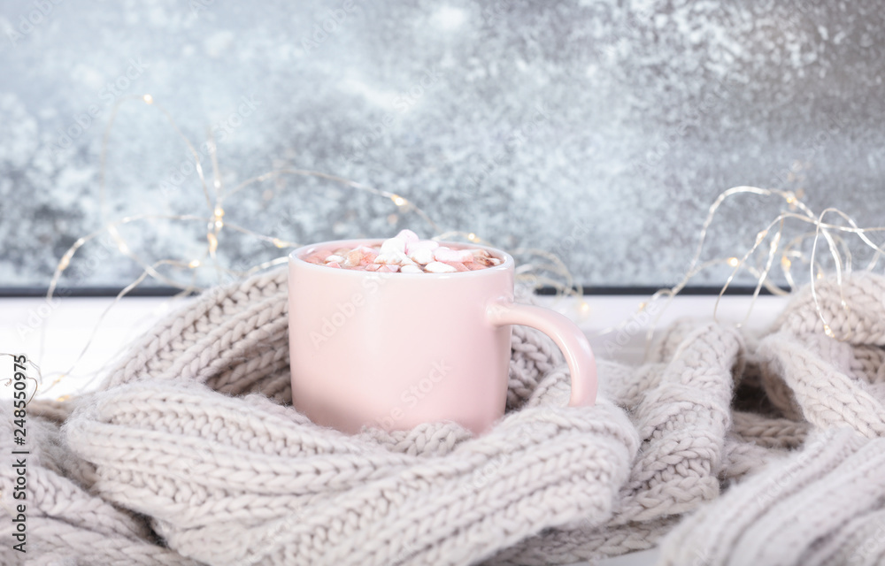Cup of aromatic cacao with marshmallows and warm scarf on window sill Cup of aromatic cacao with marshmallows and warm scarf on window sill