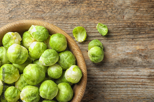 Bowl of fresh Brussels sprouts on wooden background, top view with space for text