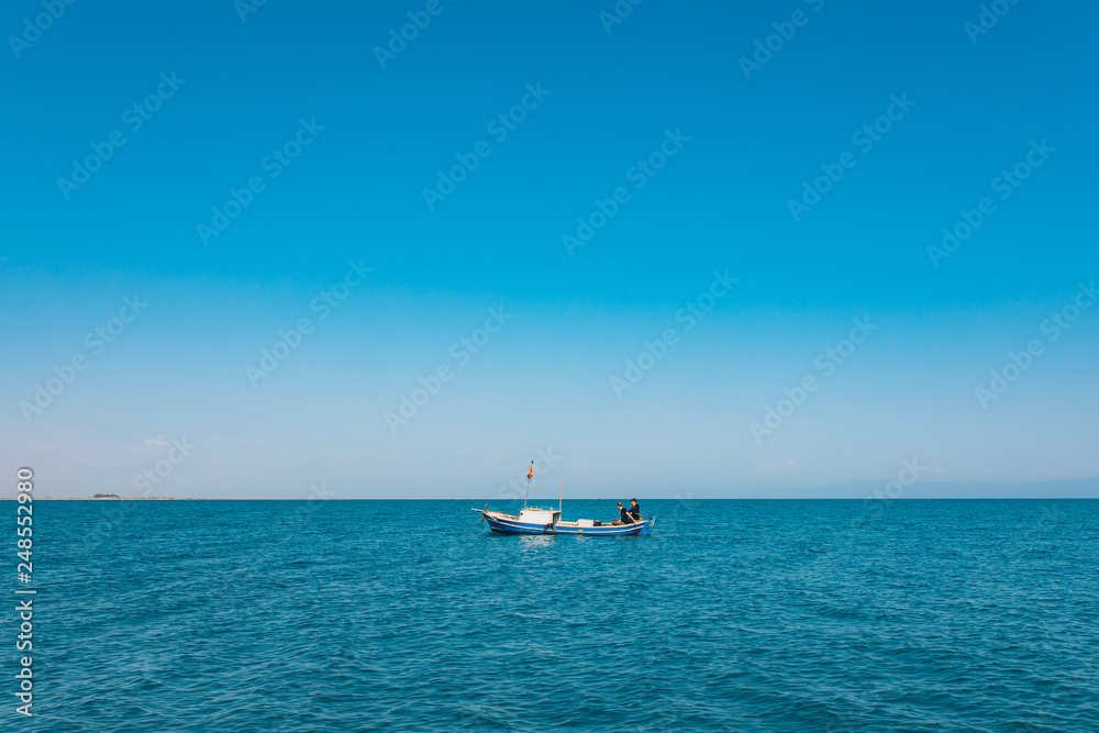 Fishermen sitting in a boat while fishing at the sea in the summer season. This fishermen in the wooden boat at the ocean. Fishing under the clean blue sky and seashore