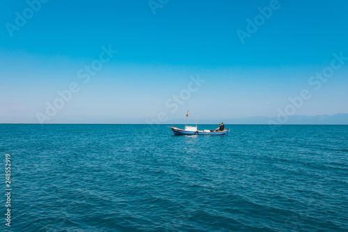 Fishermen sitting in a boat while fishing at the sea in the summer season. This fishermen in the wooden boat at the ocean. Fishing under the clean blue sky and seashore © Hakan Tanak