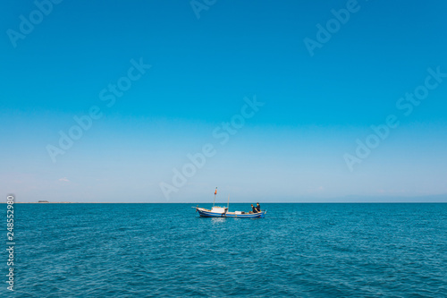 Fishermen sitting in a boat while fishing at the sea in the summer season. This fishermen in the wooden boat at the ocean. Fishing under the clean blue sky and seashore © Hakan Tanak