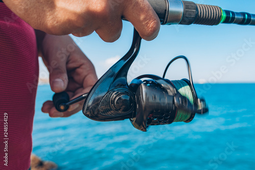 Man holding Fishing rod tackles close up. Hand with spinning reel. Fisherman standing and throw a fishing rod while fishing at the sea background.