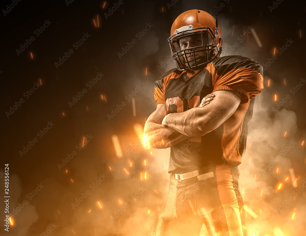 American football player on dark background in smoke and sparks in black and orange outfit.